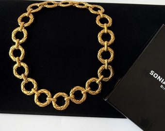 Puede incluir: Un collar de cadena de oro con un diseño tejido. El collar está hecho de grandes anillos redondos unidos.