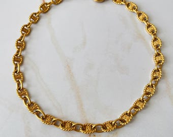 Puede incluir: Un collar de cadena de oro con un diseño detallado y texturizado. La cadena está hecha de eslabones ovalados con un borde de cuerda.
