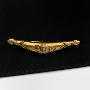 May include: A gold-toned metal hair clip with a floral design. The clip is shaped like a crescent moon and has a detailed floral pattern in the center.
