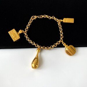 May include: A gold chain bracelet with three charms: a rectangular charm with an ornate design, a teardrop-shaped charm, and a round charm.