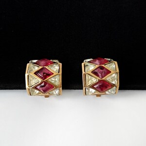 Può includere: Un paio di orecchini a clip dorati con strass rossi e trasparenti in un design geometrico.