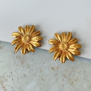 May include: A pair of gold-tone clip-on earrings shaped like sunflowers.