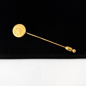 May include: A gold-coloured pin with a round head featuring the text "HERMES PARIS".
