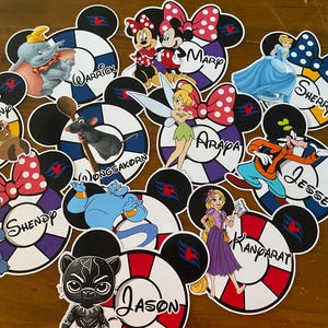 May include: A selection of Disney character cutouts. Each cutout features characters such as Dumbo, Minnie Mouse, and Cinderella, set within a Mickey Mouse head design with a life preserver motif. Names are printed on each cutout.