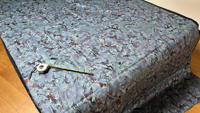 May include: A blue and green fabric with a marbled pattern. A measuring tape is lying on the fabric.