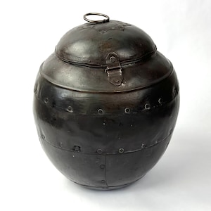 May include: A black metal jar with a hinged lid and a ring handle. The jar has a round shape and is decorated with rivets.