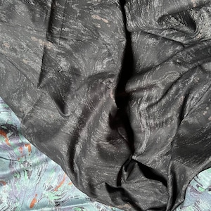 May include: A close-up of two fabric swatches. One is a black fabric with a subtle marbled pattern. The other is a light blue fabric with a marbled pattern in shades of green, purple, and orange.