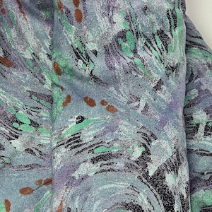 May include: A close-up of a fabric with a swirling abstract pattern in shades of blue, green, and brown. The fabric has a textured surface.