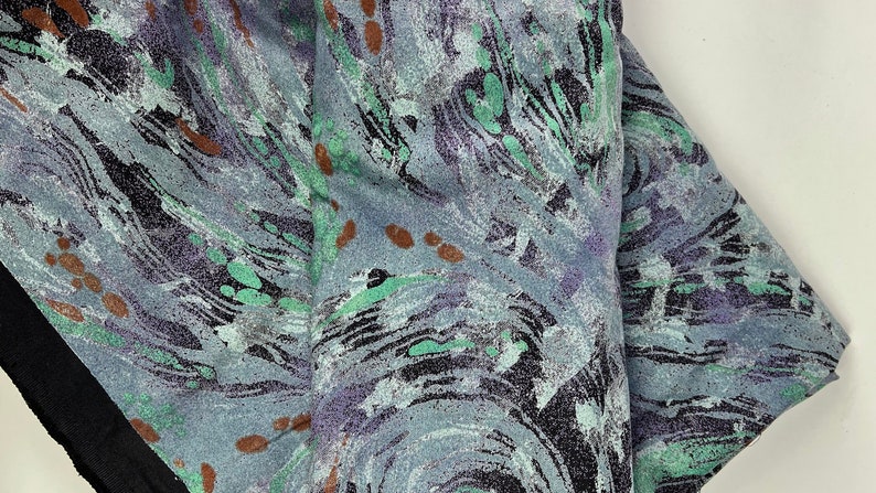 May include: A close-up of a fabric with a swirling abstract pattern in shades of blue, green, and brown. The fabric has a textured surface.