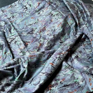 May include: A close-up of a blue, green, and brown fabric with a marbled pattern. The fabric is folded and draped, showing the texture and detail of the design.