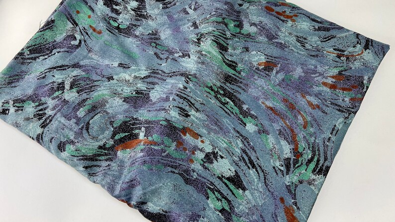 May include: A blue fabric with a swirling, abstract pattern in shades of green, purple, and brown.
