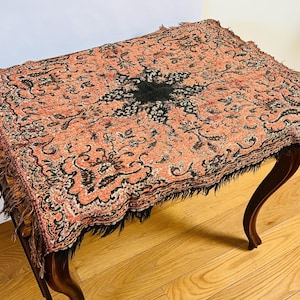 May include: A vintage table with a fringed, floral patterned tablecloth in shades of pink, black, and white.
