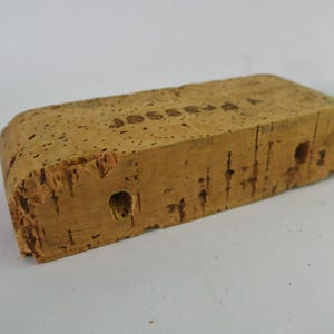 May include: A rectangular cork block with a rough, textured surface. The block has two holes and the text "JOSSERA" is stamped on the top.