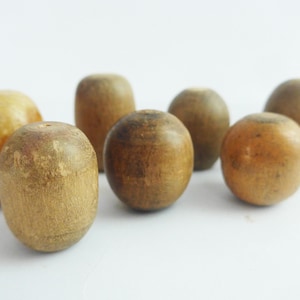 May include: A collection of seven wooden beads in various shapes and sizes. The beads range in color from light tan to dark brown, with visible wood grain. Some are cylindrical, while others are spherical.
