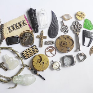 May include: A collection of vintage trinkets and charms, including a small wooden angel wing, a key, a crystal, a watch face, a cross, a small bottle, and a metal charm with a kangaroo on it.
