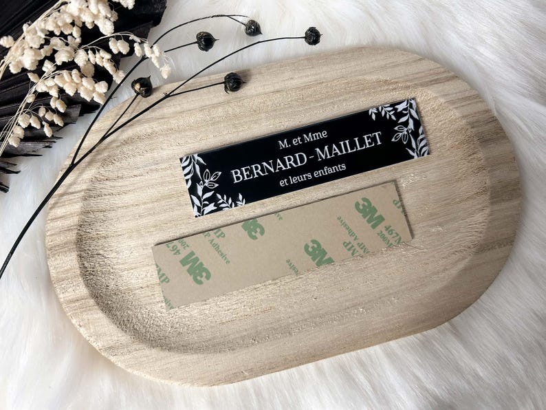 May include: A black and white sign with the text "M. et Mme BERNARD-MAILLET et leurs enfants" and a floral design. The sign is on a wooden surface with adhesive tape.
