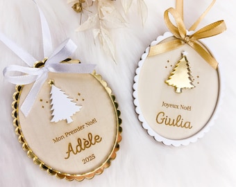 Könnte beinhalten: Zwei ovale Weihnachtsanhänger aus Holz mit gewelltem Rand. Einer hat ein weißes Band und einen Baum mit dem Text Mon Premier Noël Adèle 2025. Der andere hat ein goldenes Band und einen goldenen Baum mit dem Text Joyeux Noël Giulia. Beide haben kleine Sterne.