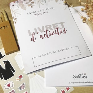K&ouml;nnte beinhalten: Ein wei&szlig;es Aktivit&auml;tsheft mit dem Titel LIVRET d'activit&eacute;s, den Namen Lauren & Steven und dem Datum 10 juin 2023. Es enth&auml;lt einen Bogen mit Hochzeitsaufklebern, die einen Smoking, ein Kleid und Blumen zeigen, sowie eine kleine Schachtel Buntstifte.