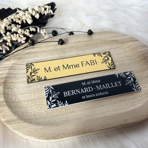 May include: Two gold and black name cards with floral designs. The top card reads "M. et Mme FABI" and the bottom card reads "M. et Mme BERNARD-MAILLET et leurs enfants".