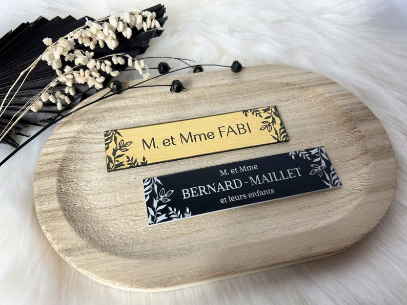 May include: Two gold and black name cards with floral designs. The top card reads "M. et Mme FABI" and the bottom card reads "M. et Mme BERNARD-MAILLET et leurs enfants".