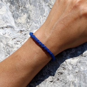 Könnte beinhalten: Ein blaues geflochtenes Armband an einem Handgelenk.