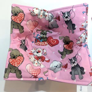 May include: Pink fabric bowl cozy with a repeating pattern of cartoon dogs, hearts, and balloons. The dogs are holding hearts and roses. The fabric is quilted with a stitched diamond pattern.