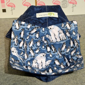 May include: A navy blue bowl cozy with a penguin and polar bear print. The interior is a solid navy blue. The cozy has a tag that says "Kozy Together".
