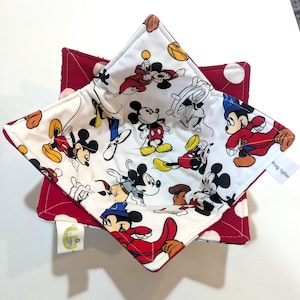 May include: A set of two square fabric bowl cozies. The top cozy features a white background with a Mickey Mouse print in various poses. The bottom cozy is red with white polka dots. The edges are red.