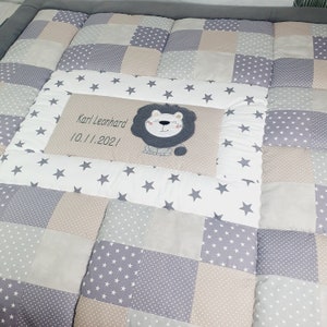 Könnte beinhalten: Eine graue und beige Patchwork-Babydecke mit einem weißen Feld, auf dem ein Löwe und der Text "Karl Leonard 10.11.2021" abgebildet sind.