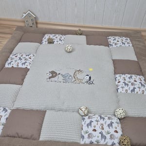 Può includere: Un tappetino da gioco trapuntato grigio e marrone con un design cucito di animali, tra cui un leone, un elefante, una giraffa e una zebra. Il tappetino è realizzato in tessuto morbido e confortevole ed è perfetto per neonati e bambini piccoli.