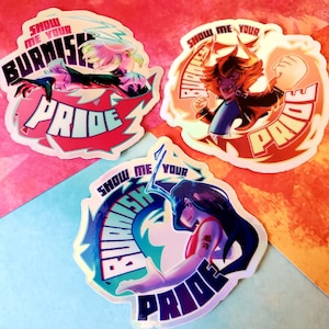 Könnte beinhalten: Drei holografische Aufkleber mit einem farbenfrohen Design. Jeder Aufkleber zeigt einen Charakter mit einem feurigen Hintergrund und dem Text "Zeig mir deinen glühenden Stolz".