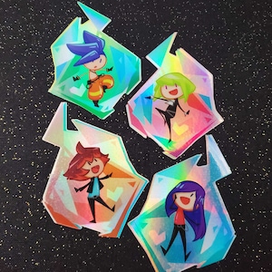 Könnte beinhalten: Vier farbige Aufkleber mit Comicfiguren in verschiedenen Posen. Jeder Aufkleber ist kristallförmig und hat eine holografische Oberfläche.