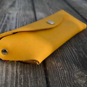 Peut inclure: Une trousse à crayons en cuir jaune avec une fermeture à pression argentée.