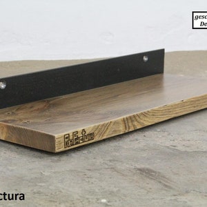 Könnte beinhalten: Ein Holzregal mit einer schwarzen Metallhalterung. Das Regal hat eine natürliche Holzoptik und die Halterung eine mattschwarze Oberfläche. Das Regal ist mit dem Text "ReFactura" beschriftet.