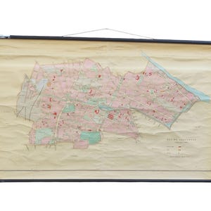 May include: Vintage city map on a cream-colored paper, mounted on black wooden rods. The map features a detailed layout with pink and green areas, likely representing buildings and parks. The map is suspended by a string.