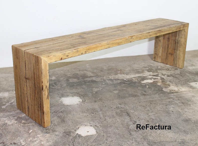 Pu&ograve; includere: Panca rustica in legno con piano rettangolare e due spessi supporti verticali. La panca &egrave; realizzata in legno di recupero, mostrando venature e nodi naturali. La panca &egrave; lunga circa 152 cm.