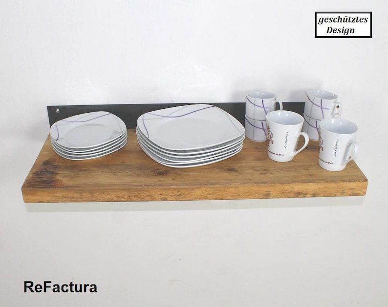 May include: A wooden shelf with a black metal bracket, holding white plates and mugs. The shelf is made of reclaimed wood and has a rustic look. The mugs have a purple and white design and the text "gesch&uuml;tztes Design" is visible in the upper right corner of the image.