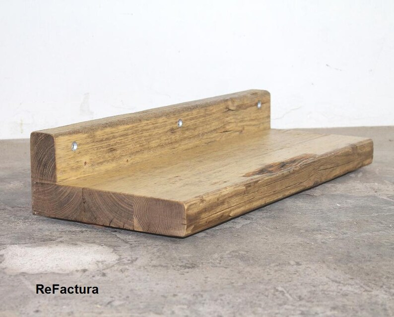 May include: A rustic wooden shelf with a natural wood finish. The shelf is made from reclaimed wood and has a unique, weathered look. It is supported by metal brackets and has a simple, minimalist design.