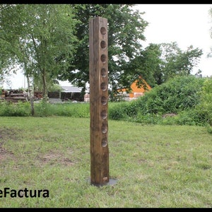 May include: A tall, wooden wine rack with 10 holes for storing wine bottles. The rack is standing on a grassy lawn.