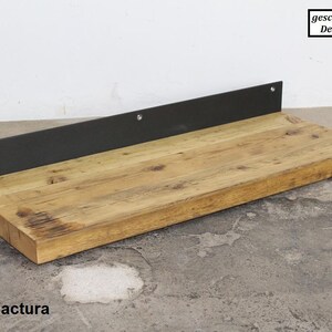 May include: A rustic wooden shelf with a black metal bracket. The shelf is made of reclaimed wood and has a natural, weathered finish. The metal bracket is attached to the underside of the shelf and has a simple, industrial design. The shelf is perfect for displaying decorative items or storing small objects.