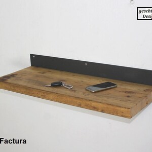 May include: A rustic wooden shelf with a black metal bracket. The shelf is mounted to a white wall and has a cell phone and keys on it. The text "gesch&uuml;tztes Design" is visible in the upper right corner of the image.