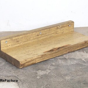 May include: A rustic wooden shelf with a natural wood finish. The shelf is mounted to a wall with screws and has a slightly uneven surface.