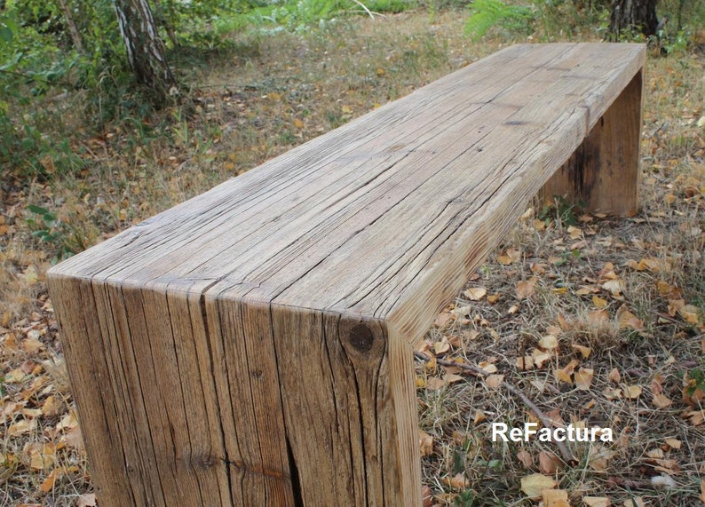 Pu&ograve; includere: Panca in legno rustico dall'aspetto naturale e invecchiato. &Egrave; costruita con spesse assi rettangolari di legno, con venature e nodi visibili. La panca &egrave; all'aperto, circondata dal fogliame.