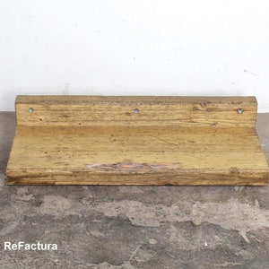 May include: A rustic wooden shelf with a natural wood finish. The shelf has a slightly uneven surface and is mounted to a wall with metal brackets. The shelf is approximately 12 inches wide and 6 inches deep.