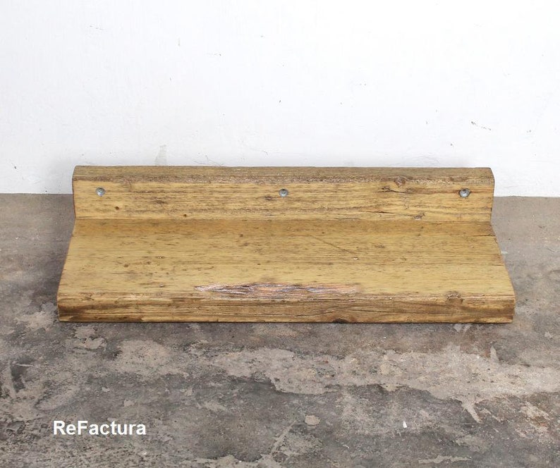 May include: A rustic wooden shelf with a natural wood finish. The shelf has a slightly uneven surface and is mounted to a wall with metal brackets. The shelf is approximately 12 inches wide and 6 inches deep.