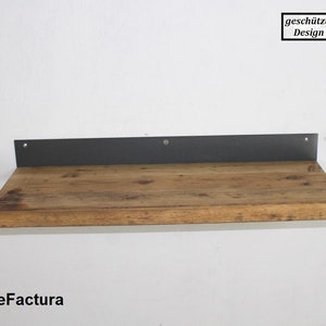 May include: A wooden shelf with a black metal bracket. The shelf is made of reclaimed wood and has a rustic look. The bracket is attached to the wall with screws. The shelf is labeled "ReFactura" in the bottom left corner. The text "gesch&uuml;tztes Design" is in a white rectangle in the top right corner.
