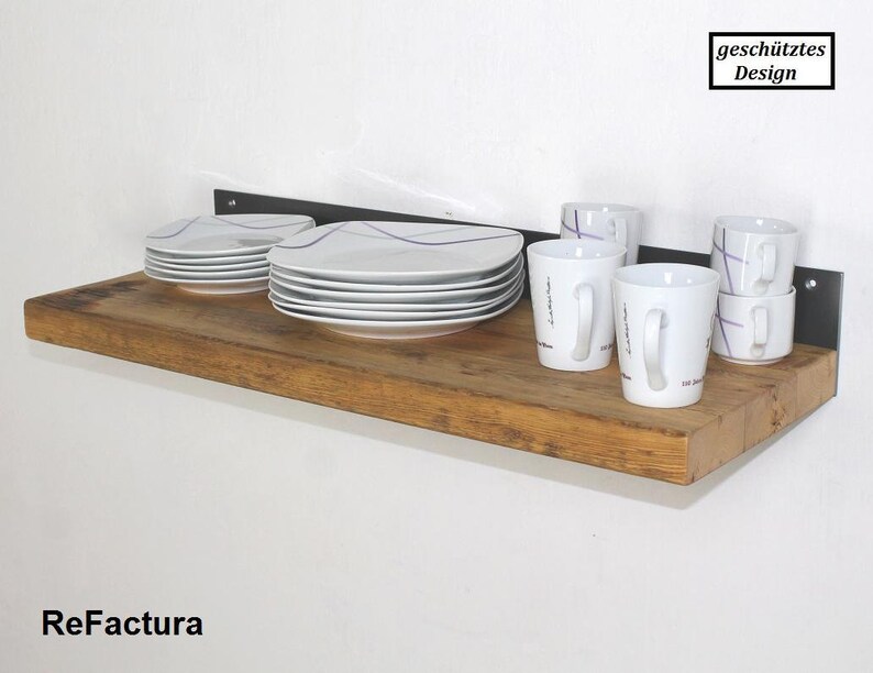 May include: A wooden shelf with a black metal bracket, holding white plates and mugs with purple designs. The shelf is labeled "ReFactura" and the bracket has a "gesch&uuml;tztes Design" label.
