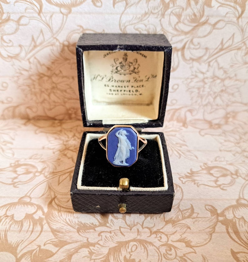 K&ouml;nnte beinhalten: Ein blauer Kameenring mit einer goldenen Fassung, der eine Frau in einem wei&szlig;en Kleid zeigt, in einer schwarzen Ringbox mit dem Text "H. Brown & Son Ltd. 65 Market Place, Sheffield. 120 at London, W."
