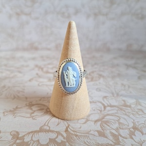 Può includere: Un anello d'argento con un cammeo blu e bianco raffigurante una donna e un cane. Il cammeo è incastonato in una lunetta ovale.