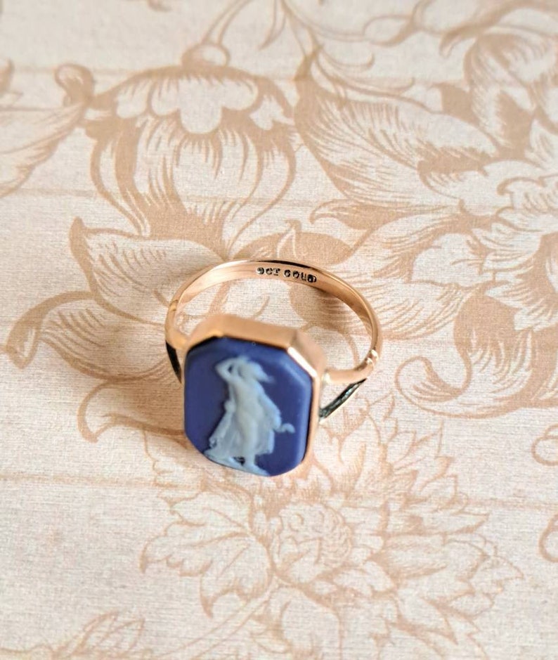 K&ouml;nnte beinhalten: Ein goldener Ring mit einem blauen Kamee, der eine Frau in einem wei&szlig;en Kleid zeigt. Der Ring ist mit "9ct GOLD 336" beschriftet.